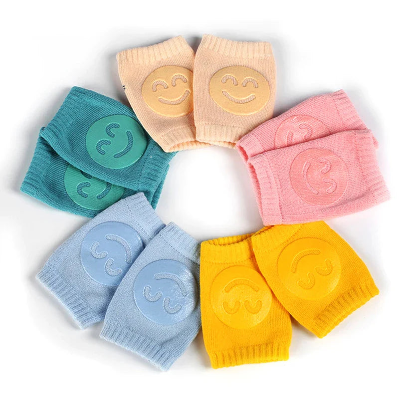 Non-slip baby knee pad in pink cotton with smiley face design, stacked with colorful pads for toddler protection during crawling.