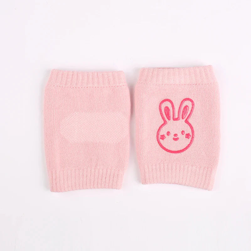 Non-slip baby knee pad in pink cotton with smiley face design, stacked with colorful pads for toddler protection during crawling.