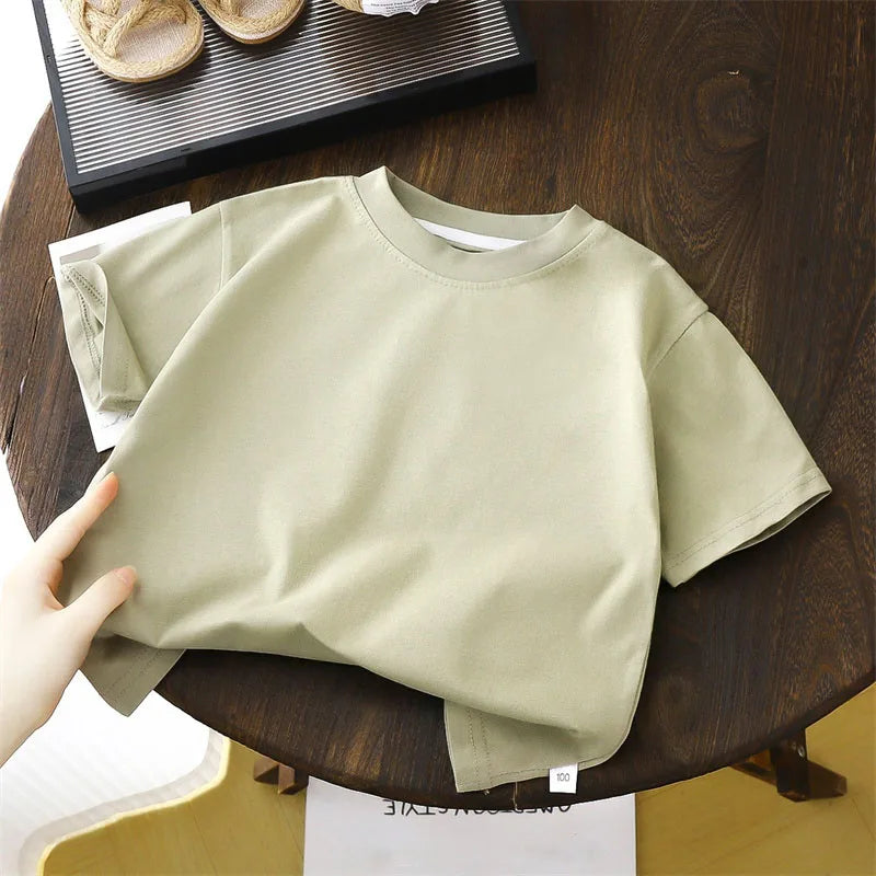 Solid cotton casual short sleeve T-shirts for kids in black, red, beige, and white colors, displayed on a wooden table.