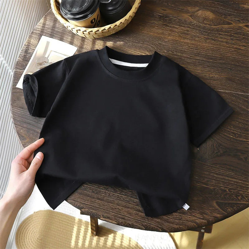 Solid cotton casual short sleeve T-shirts for kids in black, red, beige, and white colors, displayed on a wooden table.