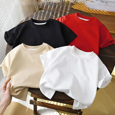 Solid cotton casual short sleeve T-shirts for kids in black, red, beige, and white colors, displayed on a wooden table.