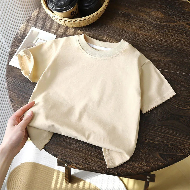 Solid cotton casual short sleeve T-shirts for kids in black, red, beige, and white colors, displayed on a wooden table.