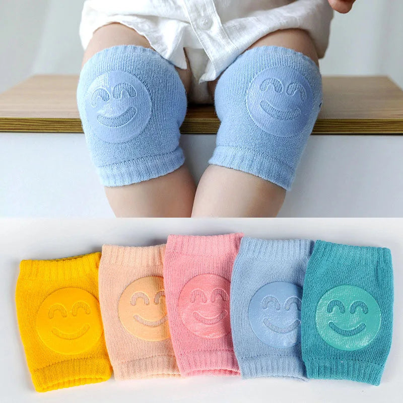 Non-slip baby knee pad in pink cotton with smiley face design, stacked with colorful pads for toddler protection during crawling.