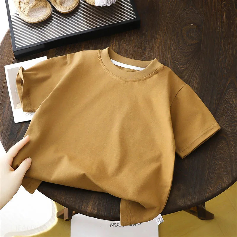 Solid cotton casual short sleeve T-shirts for kids in black, red, beige, and white colors, displayed on a wooden table.