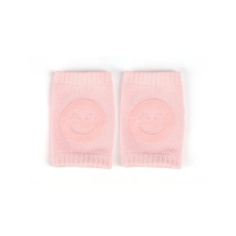 Non-slip baby knee pad in pink cotton with smiley face design, stacked with colorful pads for toddler protection during crawling.