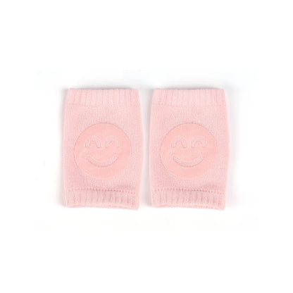 Non-slip baby knee pad in pink cotton with smiley face design, stacked with colorful pads for toddler protection during crawling.