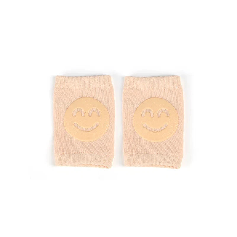 Non-slip baby knee pad in pink cotton with smiley face design, stacked with colorful pads for toddler protection during crawling.